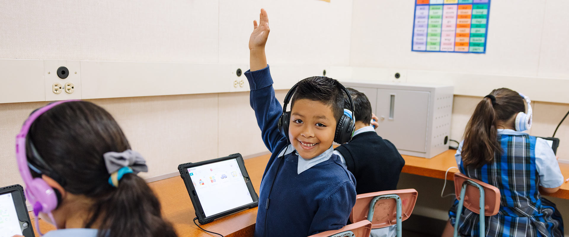 St. Raphael student learning on tablet raises hand